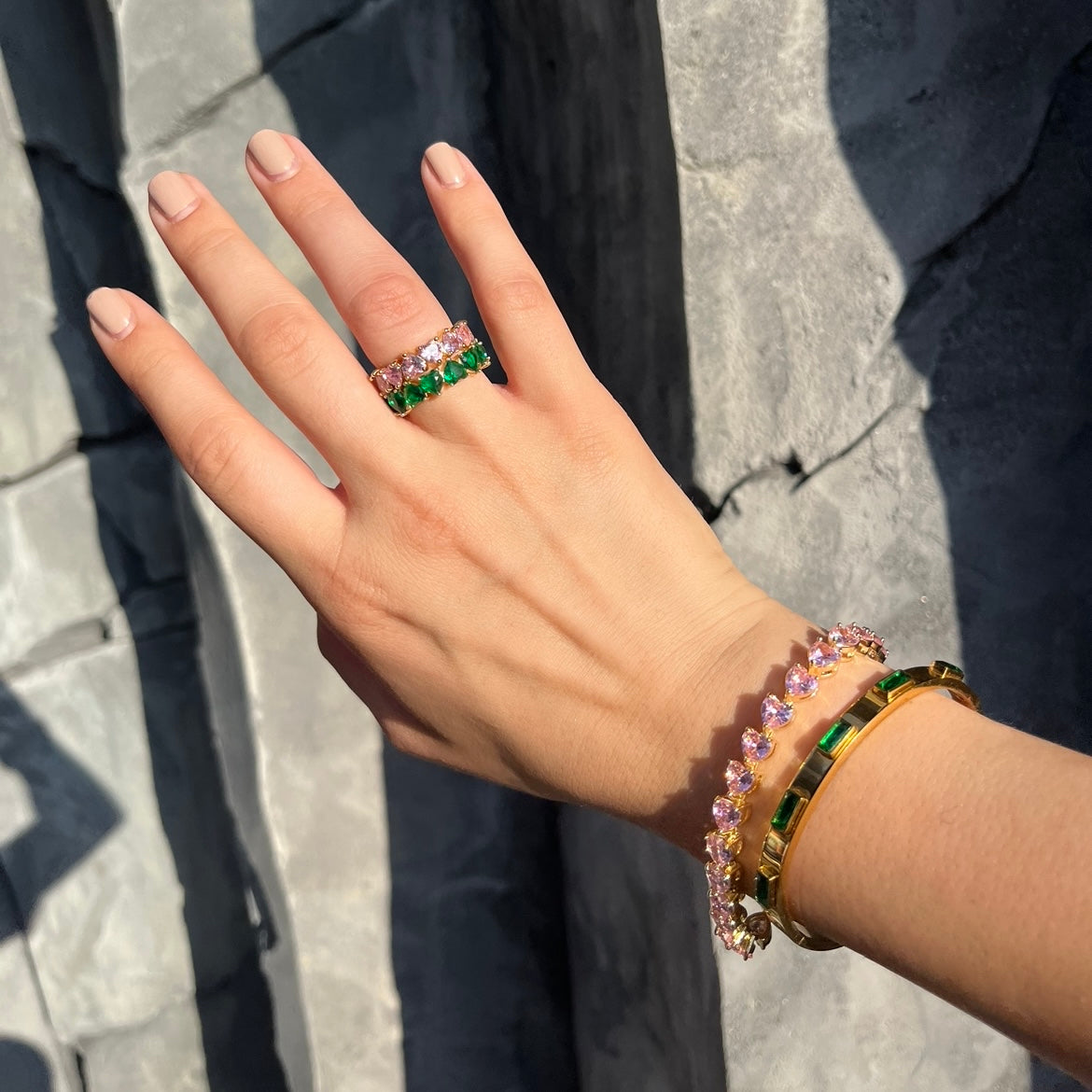 Eleganter goldener Armreif mit breite von 6mm. Er ist gleichmäßig mit hochwertigen grünen Zirkonia steinen besetzt, die sind rechteckig und leuchten in einem wunderschönen dunkel grün und sehen aus wie Smaragde. Das Armband passt perfekt in den Alltag von eleganten Frauen. Daneben ist rosa Tennis Armband mit herzförmigen zirkonia.