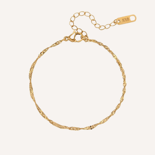 Klassisches und Zeitloses dünnes Armband in Gold. Ist in sich gedreht, diese form von kette wird Singapur genannt. Es hat ein Verlängerungskettchen mit einem rechteckigen Anhänger. Dieser Anhänger ist eingraviert mit 18K. Das Armband besteht aus Rostfreiem Stahl und ist mit 18K Gold vergoldet.