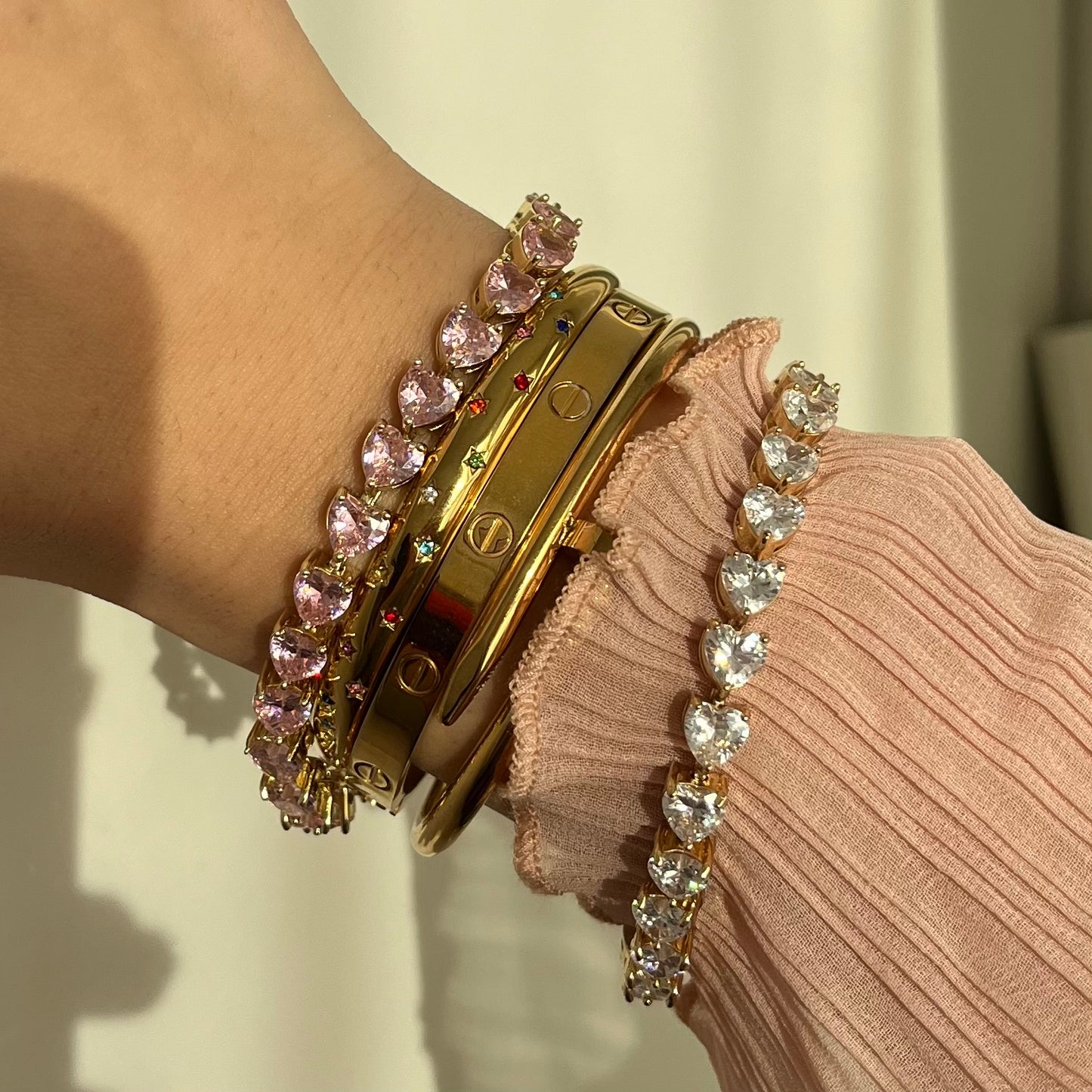 Rosa tennis Armband mit Zirkonia Herzen in gold, neben elegantem goldenen Armreif mit bunten zirkonia Sternen.